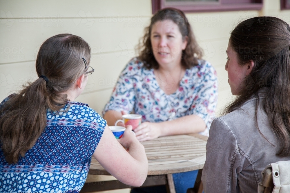 Mother and two teenage daughters sitting together talking - Australian Stock Image