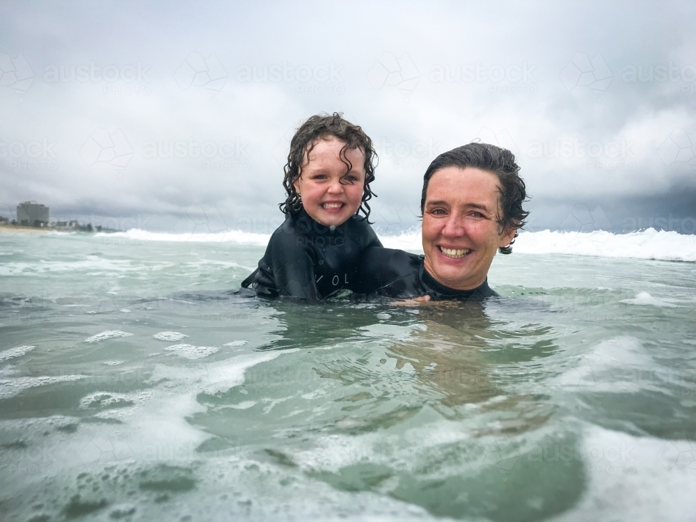 Mother and young daughter in wetsuits playing in the shores at the beach - Australian Stock Image