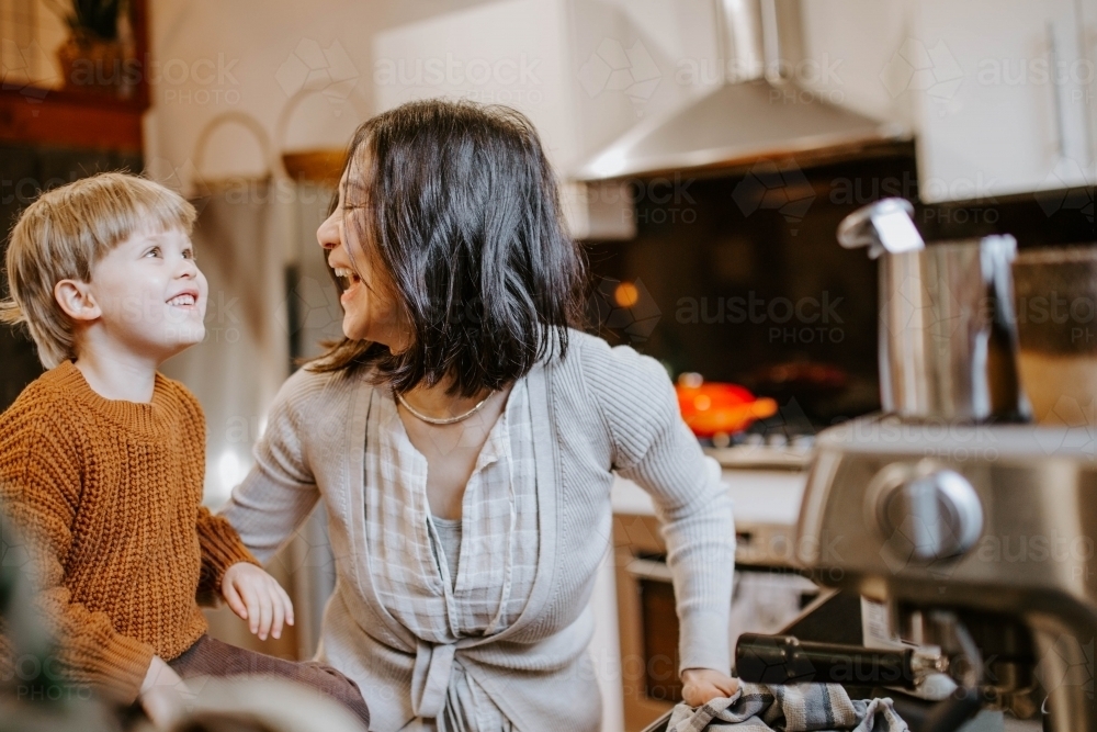 Mother and young son laughing together in home kitchen - Australian Stock Image