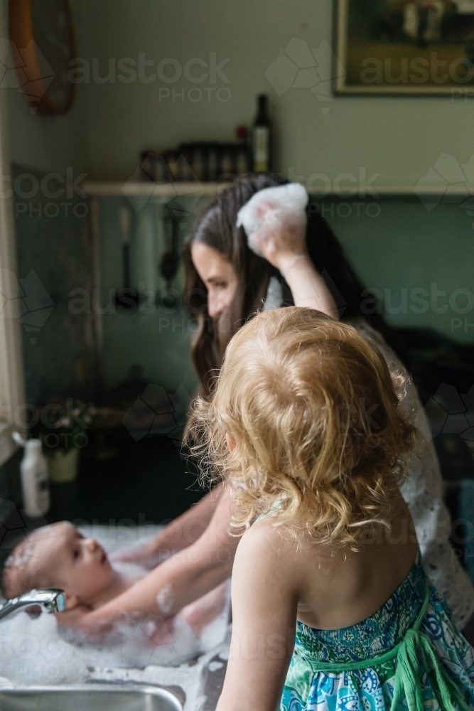 Mother bathing baby in the kitchen sink - Australian Stock Image