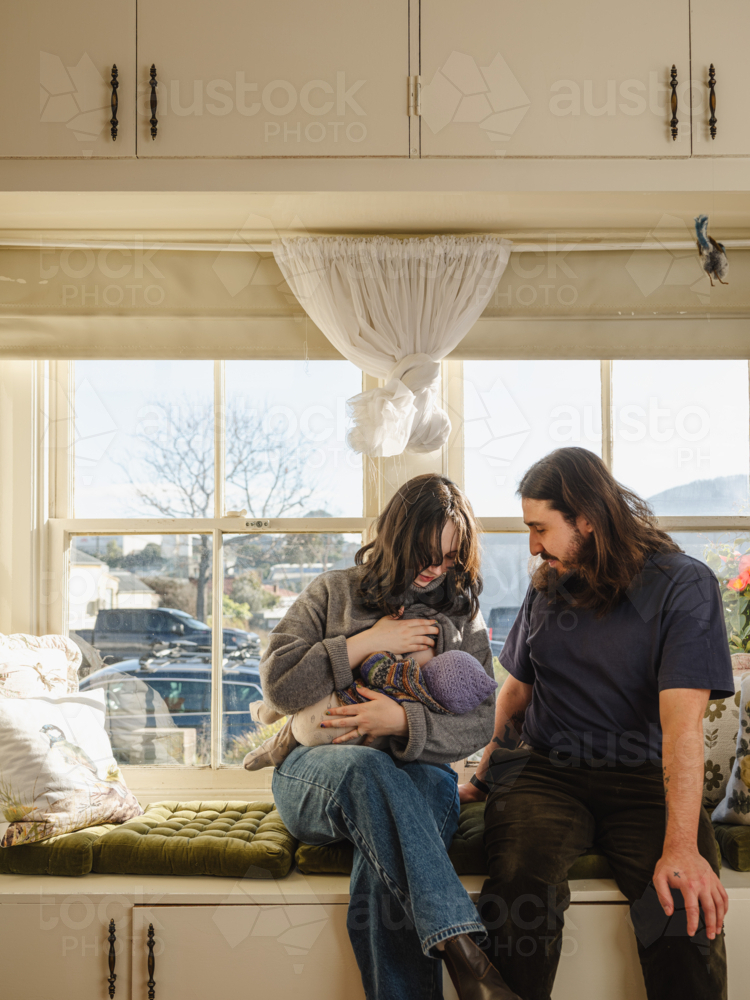 Mother breastfeeding baby wearing beanie on window seat - Australian Stock Image