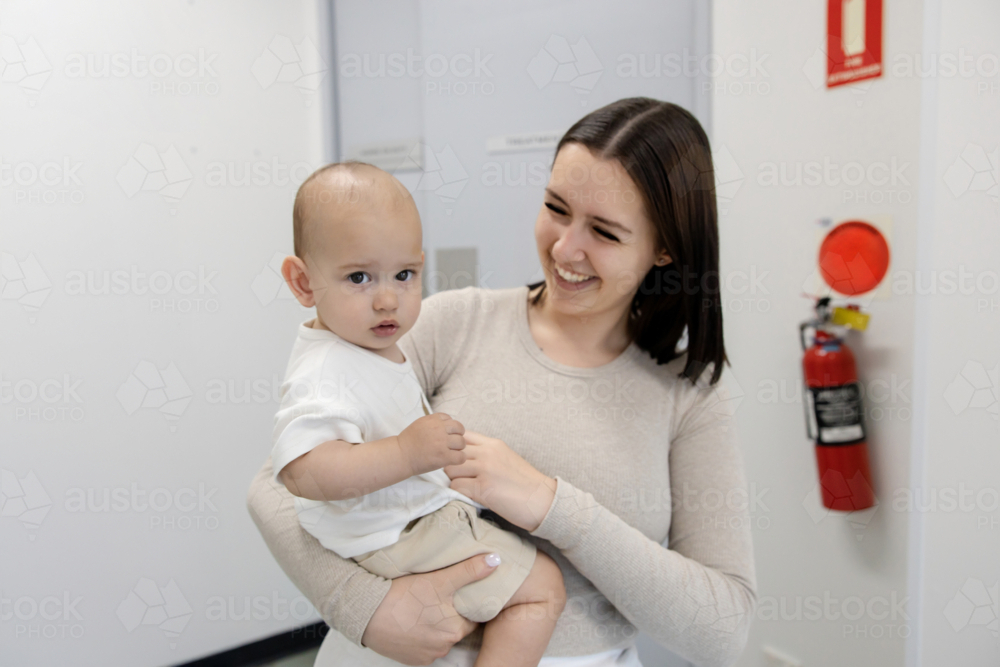 Mother carrying toddler son inside healthcare facility - Australian Stock Image