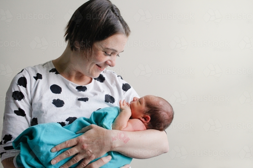 Mother cradling and smiling down at newborn baby - Australian Stock Image