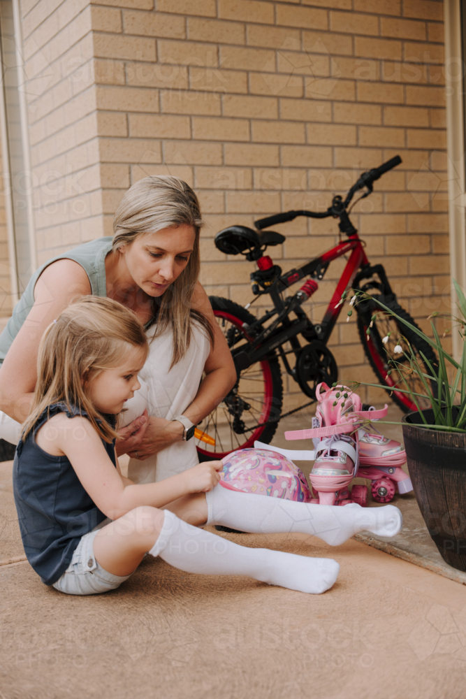 Mother crouching beside her daughter putting on her socks. - Australian Stock Image
