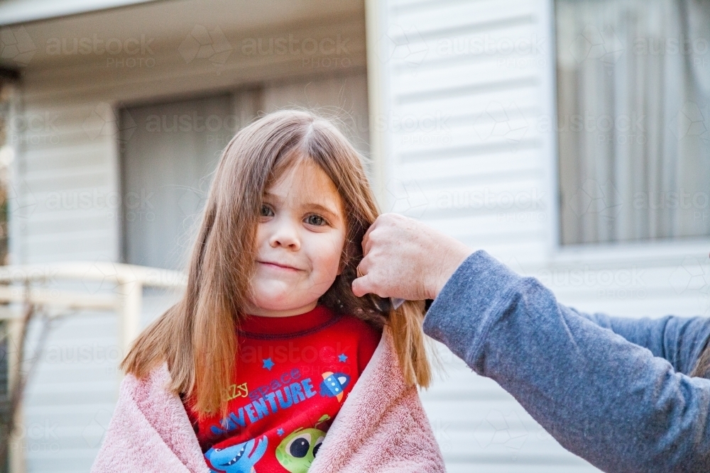 Mother cutting little girl's hair at home - Australian Stock Image