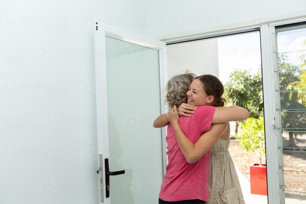 Mother embracing teen daughter at front door - Australian Stock Image