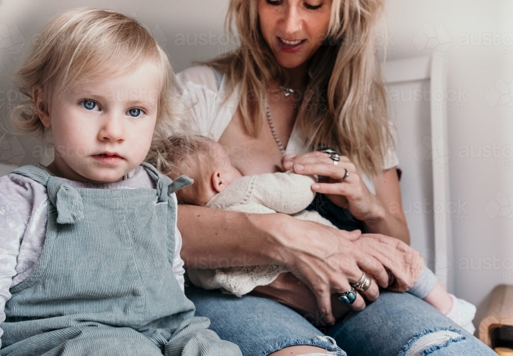 Mother feeding baby with toddler beside her. - Australian Stock Image