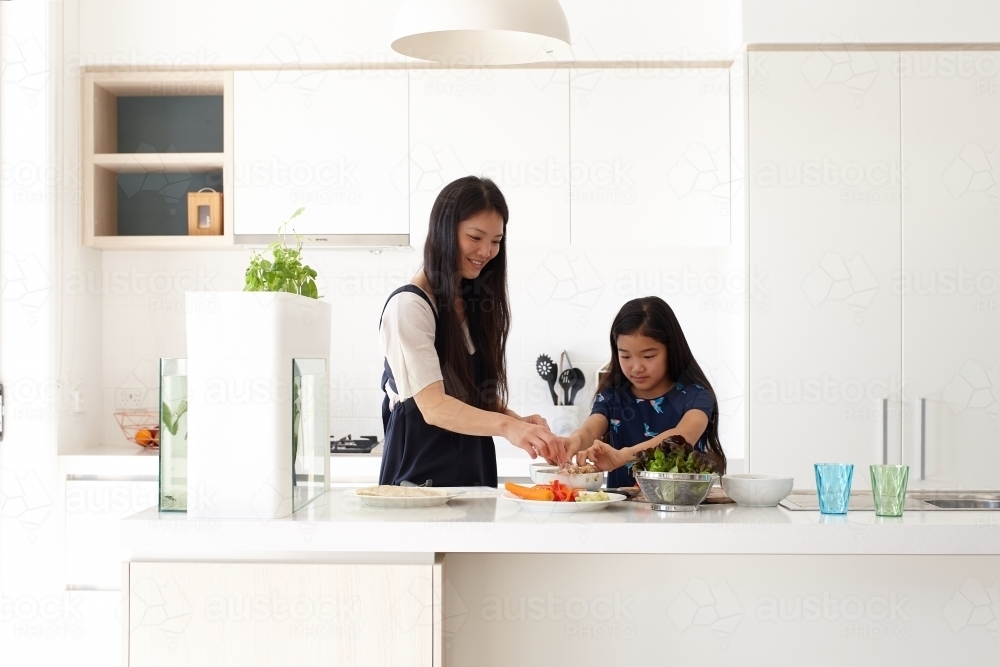 Mother helping daughter prepare a meal in kitchen - Australian Stock Image