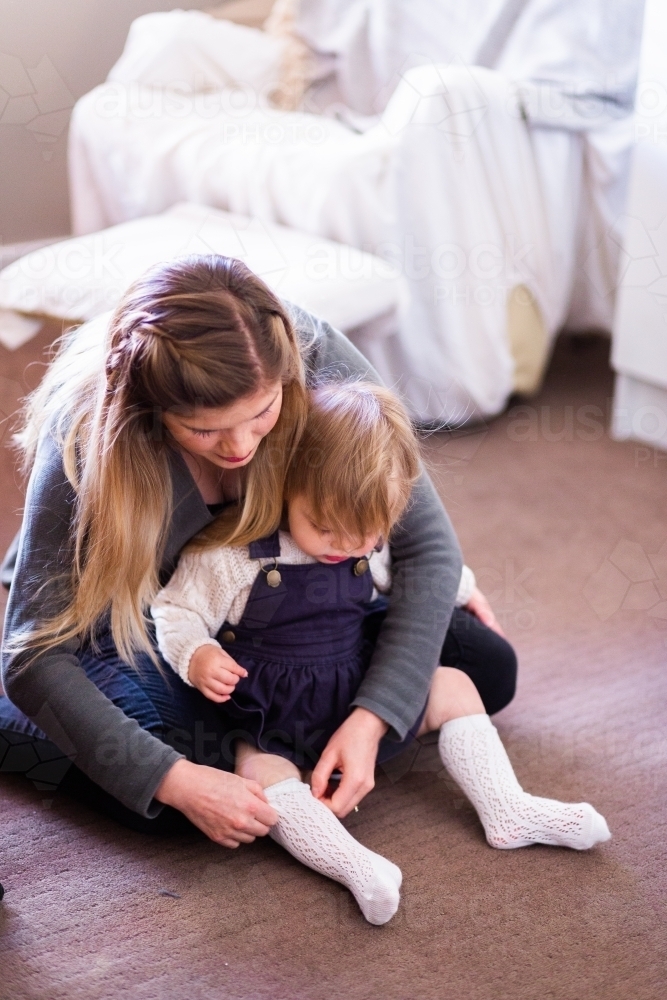 Mother helping little girl get dressed putting socks on - Australian Stock Image