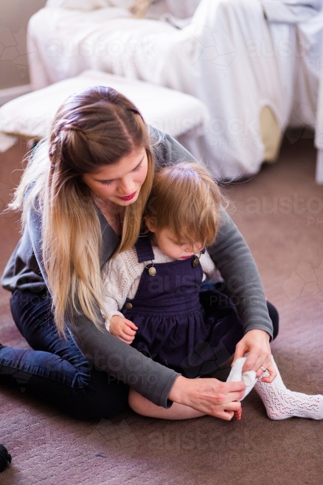 Mother helping little girl get dressed putting socks on - Australian Stock Image