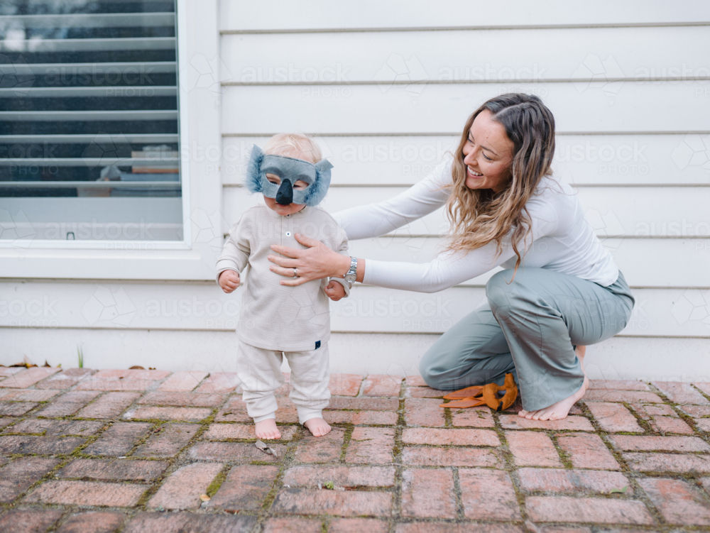 Mother holding and guiding toddler son wearing koala mask - Australian Stock Image
