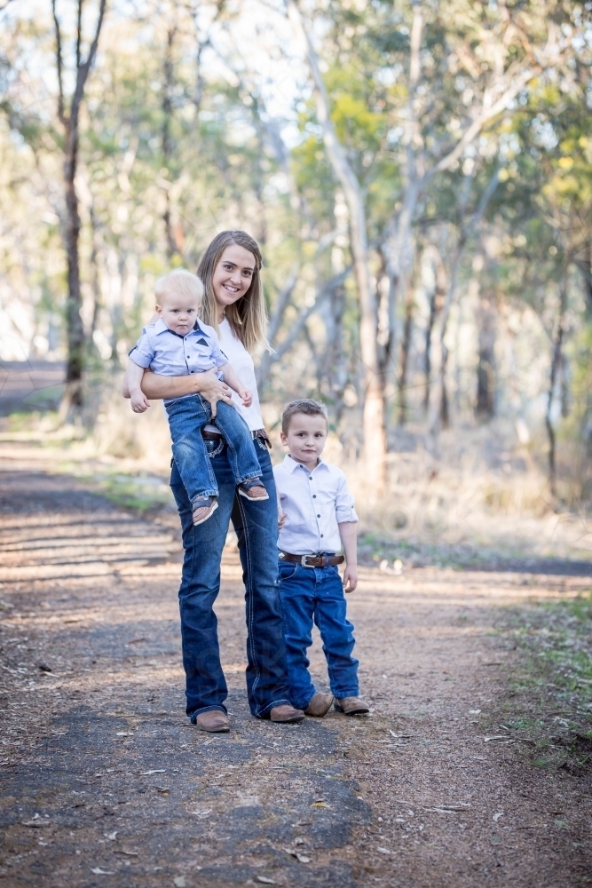 Mother holding baby boy with young son standing next to her - Australian Stock Image