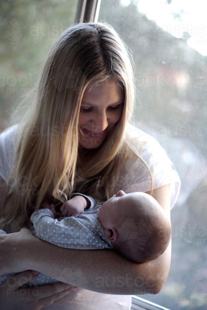 Mother holding baby by a window - Australian Stock Image