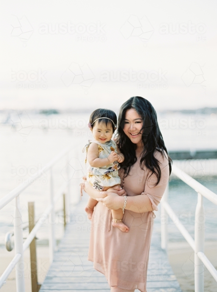 Mother holding baby girl on a wharf at the beach - Australian Stock Image