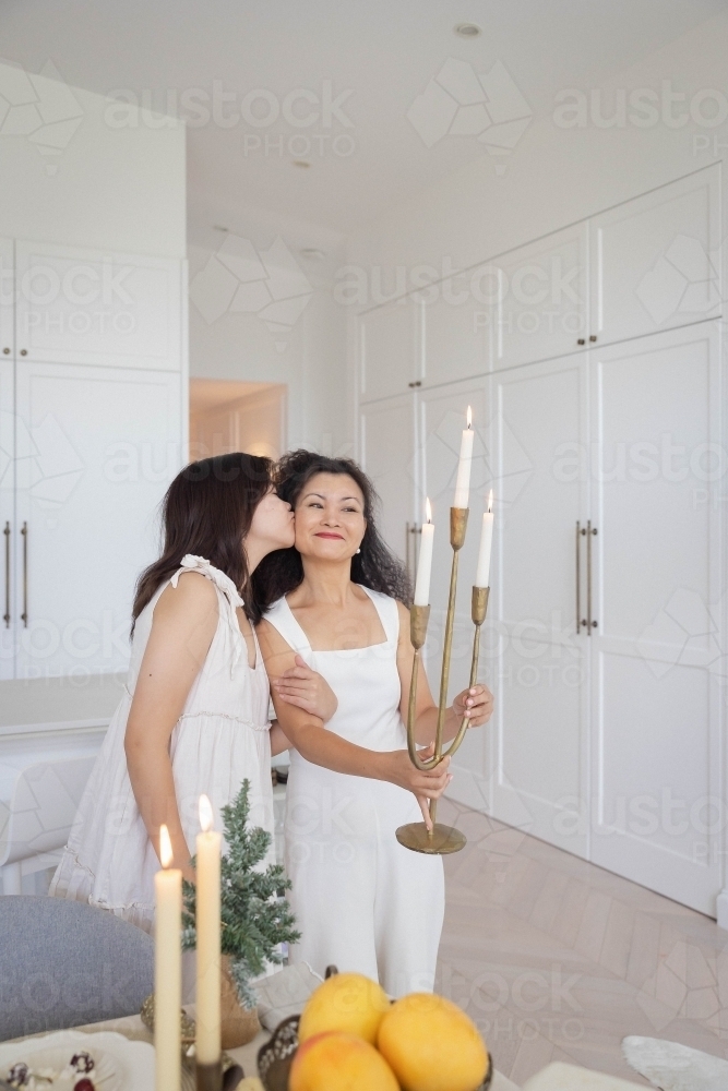 Mother holding candelabra with daughter kissing her cheek - Australian Stock Image