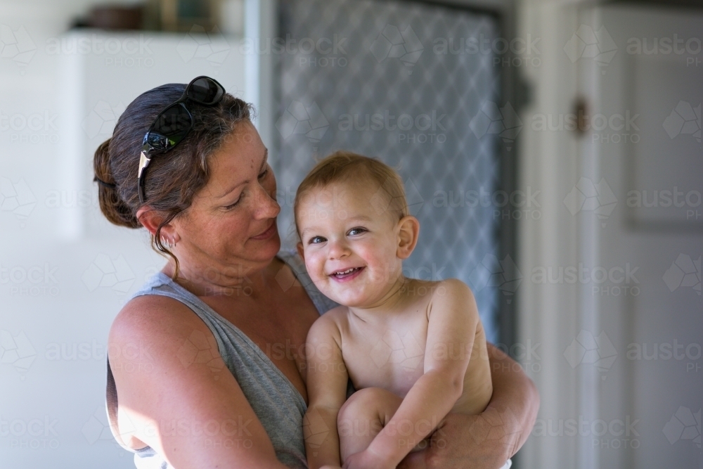 Mother holding cheerful toddler outside house - Australian Stock Image