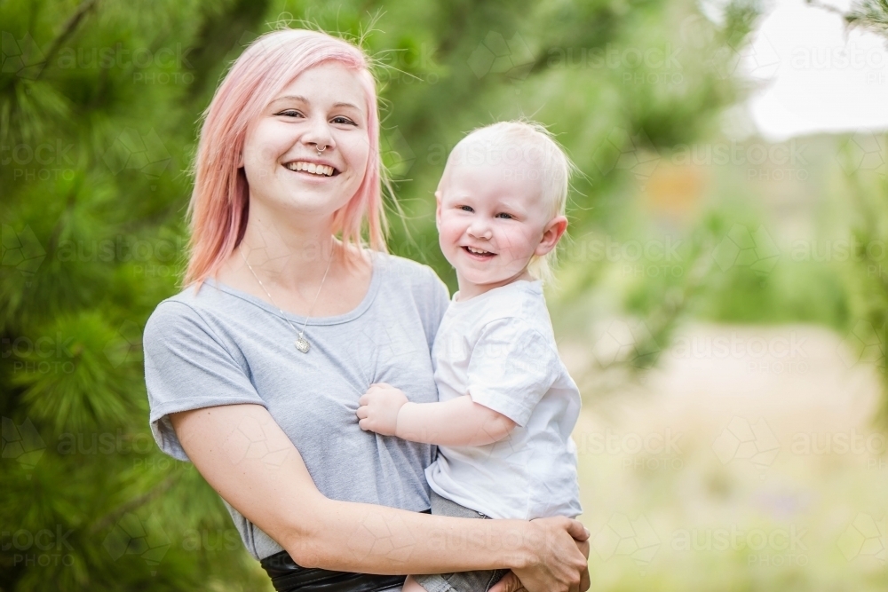 Mother holding child on hip both looking and smiling - Australian Stock Image