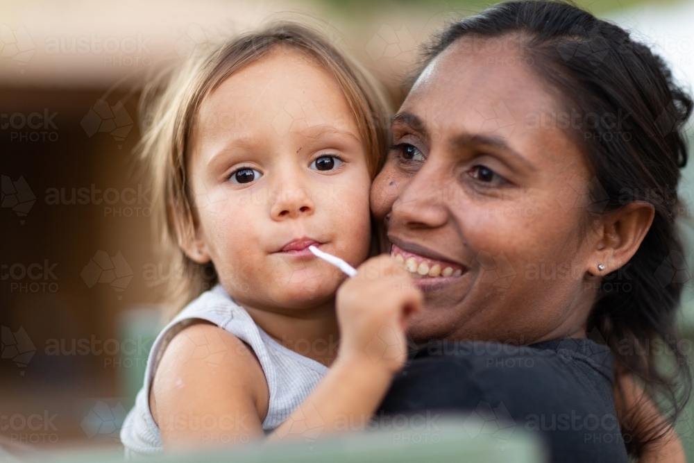 mother holding child sucking on lollipop - Australian Stock Image