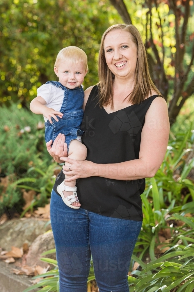 Mother holding daughter on hip smiling in garden - Australian Stock Image