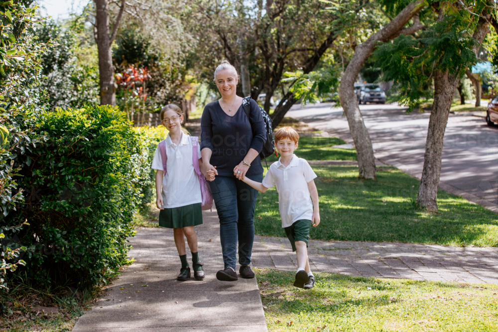 Mother holding hands with her children on footpath before school - Australian Stock Image