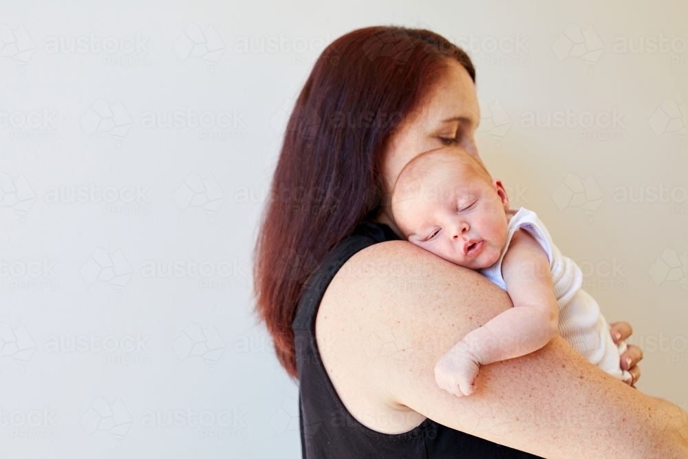 Mother holding newborn baby asleep on her shoulder - Australian Stock Image