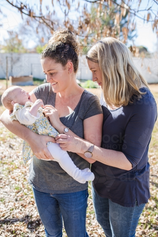 Mother holding newborn baby girl with grandmother looking and smiling - Australian Stock Image