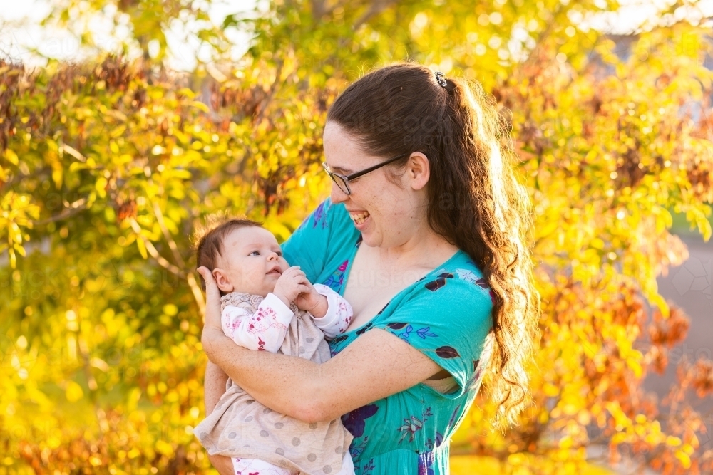 mother holding young two month old baby outside in autumn light - Australian Stock Image