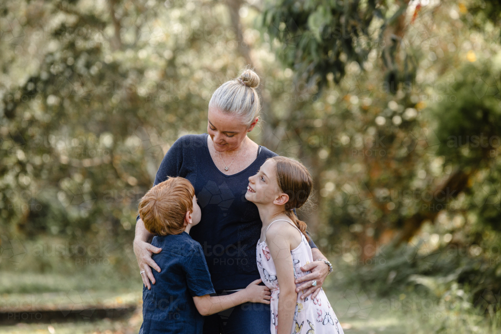 Mother hugging children while looking at her son in bushland - Australian Stock Image