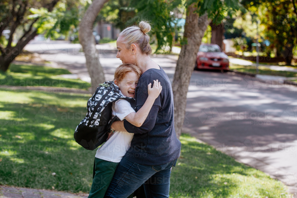 Mother hugging happy young schoolboy outdoors. - Australian Stock Image