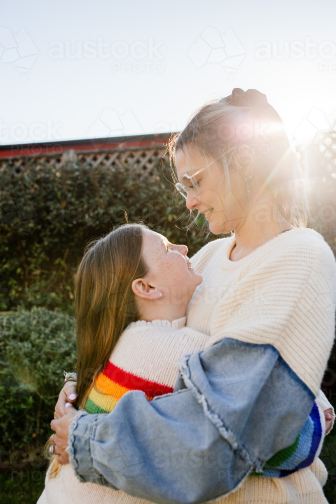 Mother hugging preteen daughter in the garden - Australian Stock Image