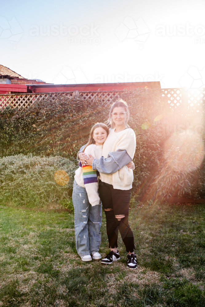 Mother hugging preteen daughter in the garden - Australian Stock Image