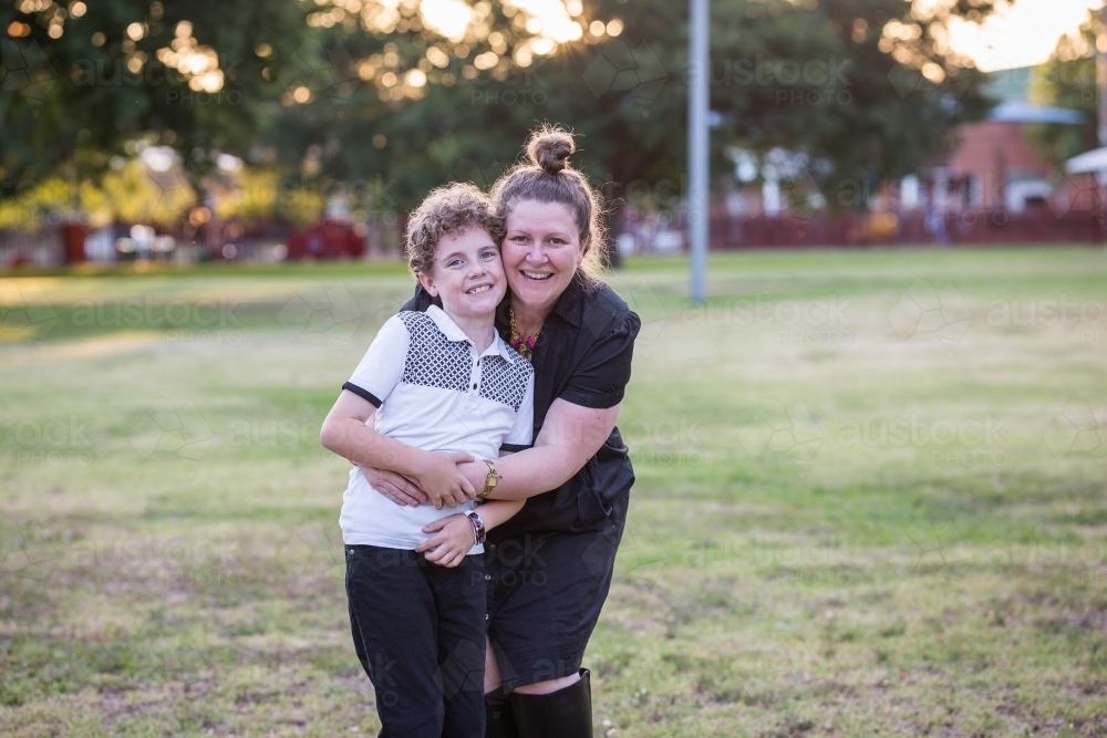 Mother hugging son from behind smiling - Australian Stock Image