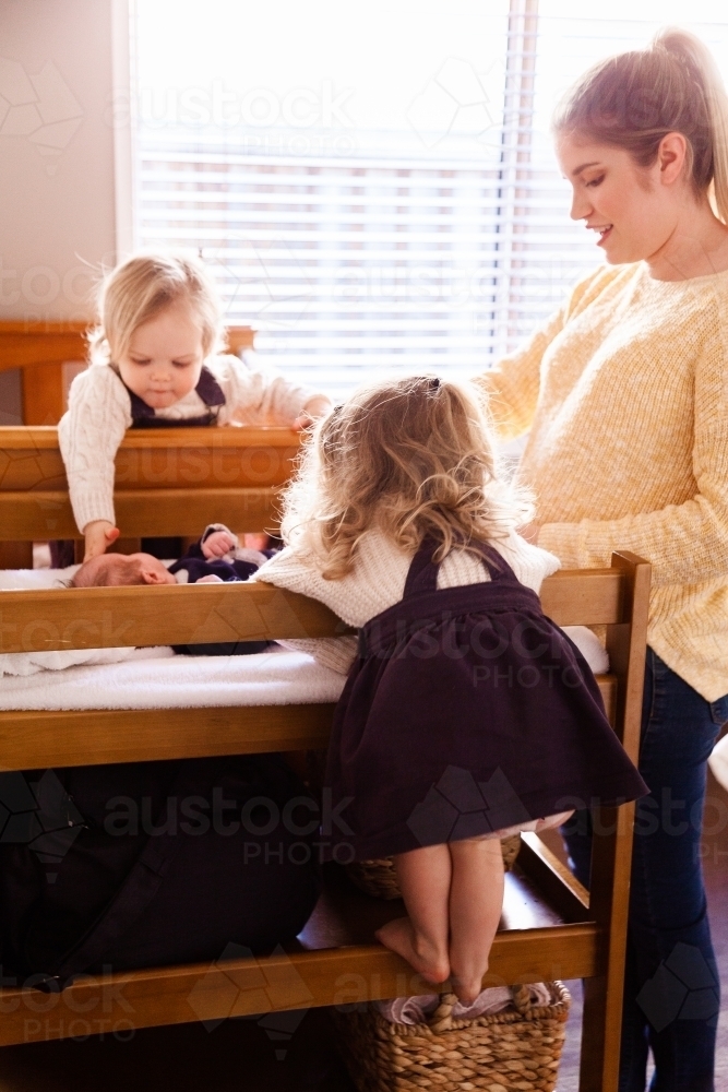 Mother in baby's room getting baby dressed sisters helping - Australian Stock Image