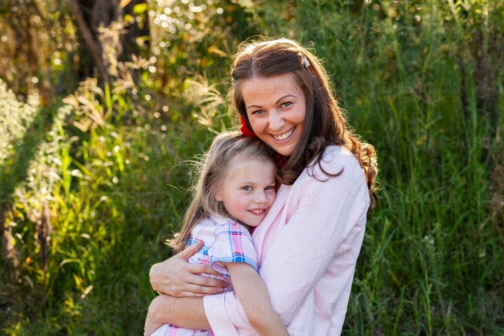 Mother in her early thirties and young daughter hug outside - Australian Stock Image