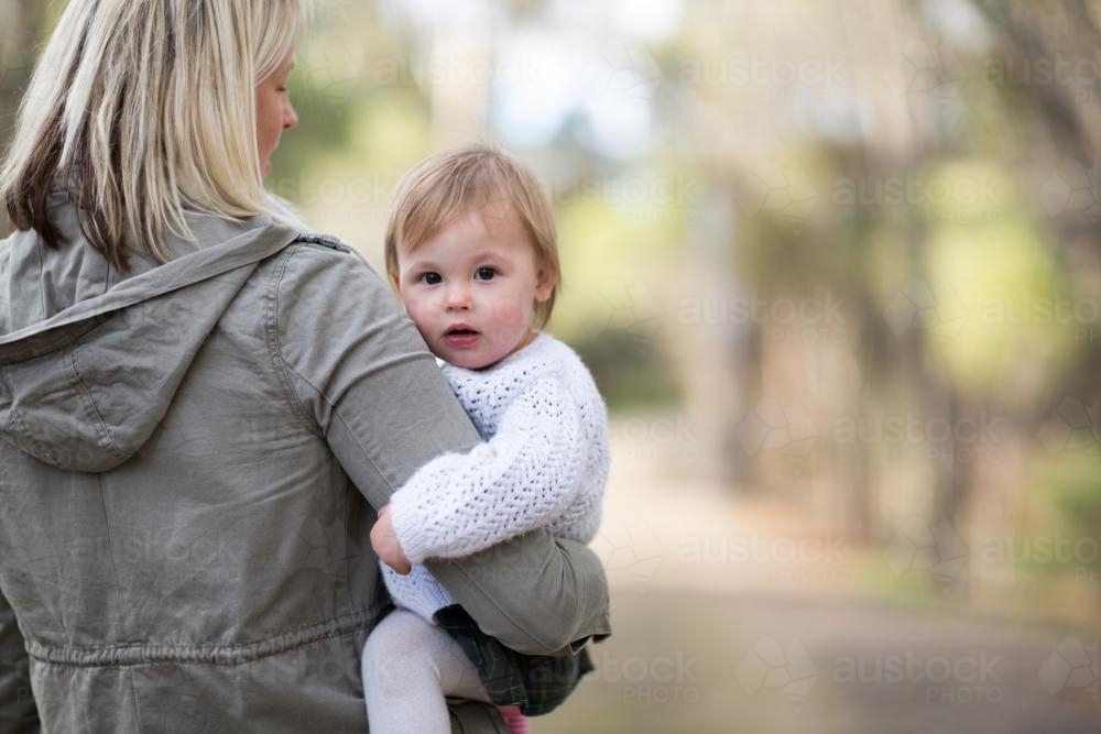 Mother in jacket carrying baby daughter on her hip - Australian Stock Image