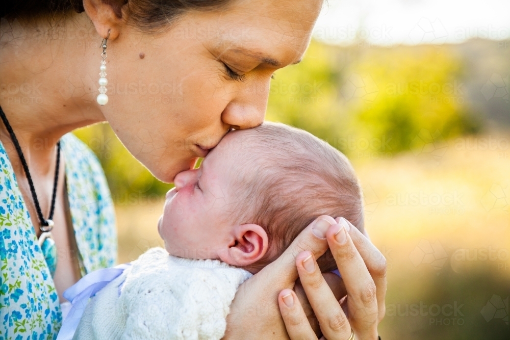 Mother kissing baby child in forehead - Australian Stock Image