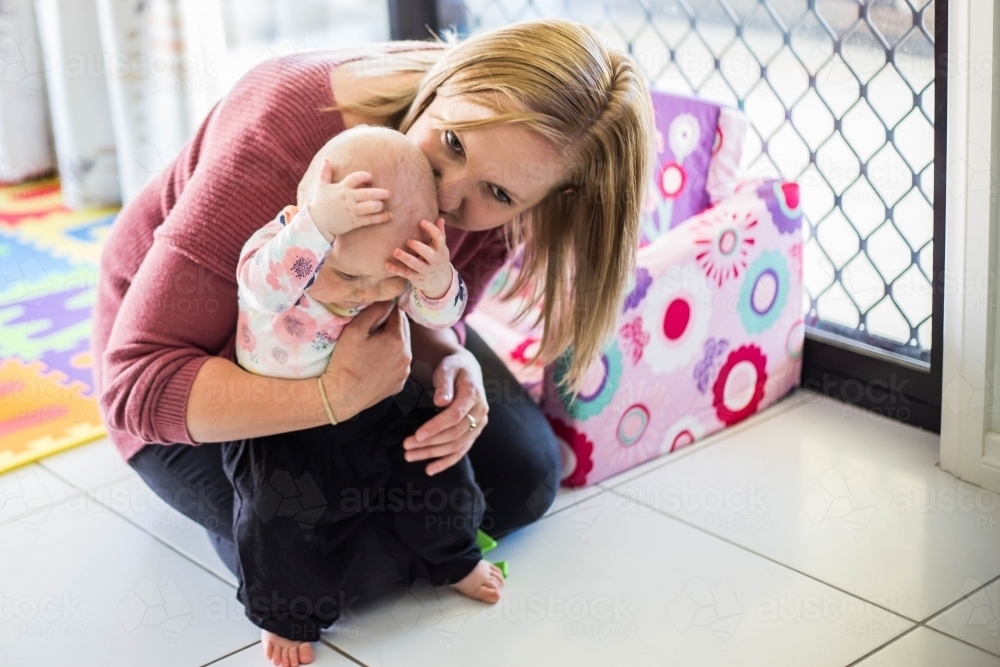 Mother kissing child's head while child sits on her lap - Australian Stock Image