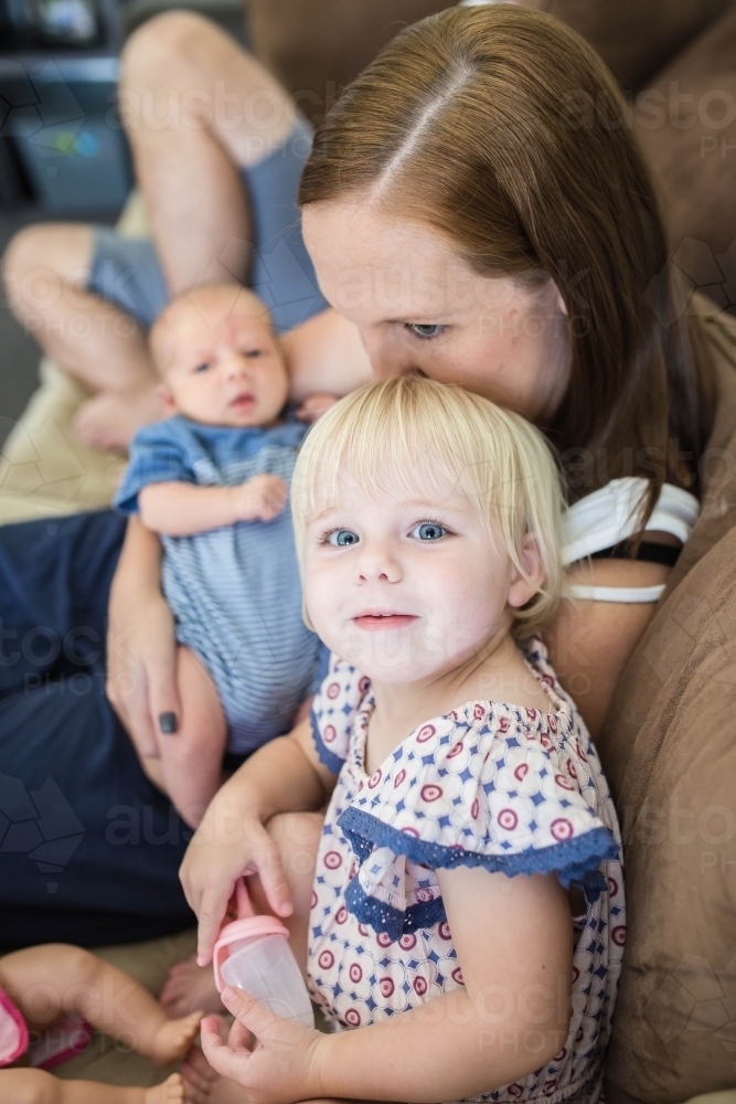 Mother kissing daughter on top of head while holding newborn baby boy - Australian Stock Image