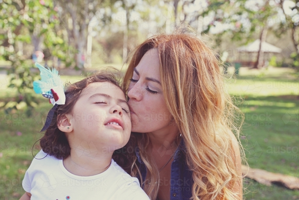 Mother kissing her little girl in the park - Australian Stock Image