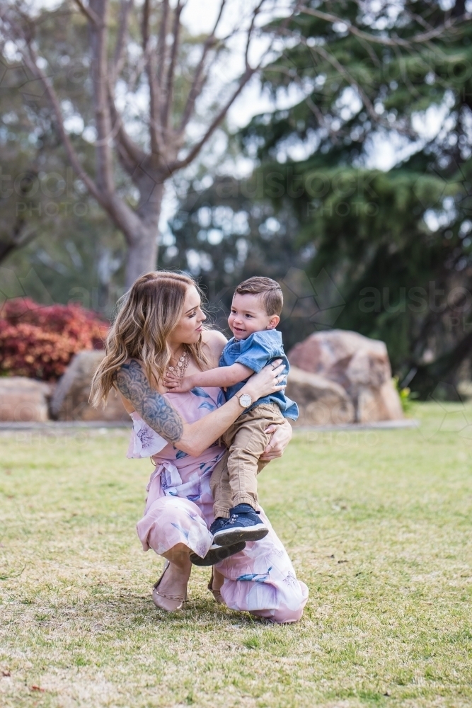 Mother kneeling down smiling at mixed race aboriginal caucasian boy in arms - Australian Stock Image