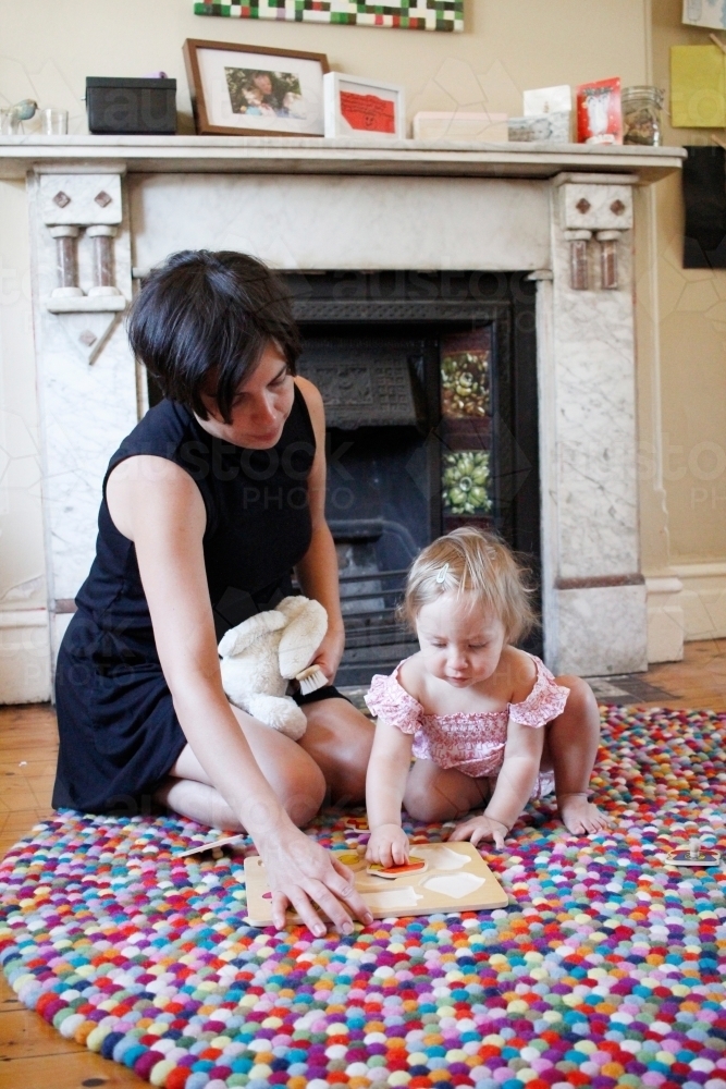 Mother kneeling on floor with her baby girl doing a puzzle - Australian Stock Image