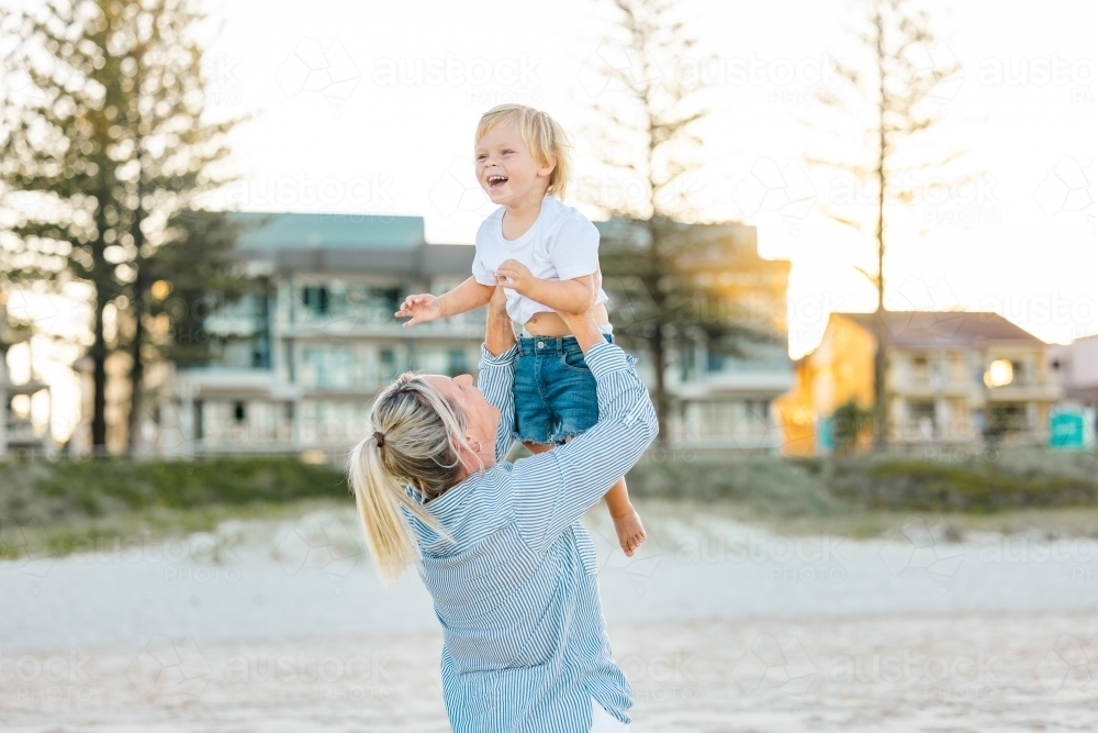 Mother lifting toddler son, playing on Gold Coast beach - Australian Stock Image