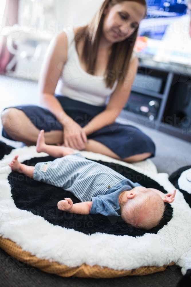 Mother looking at newborn baby boy lying on mat at home - Australian Stock Image
