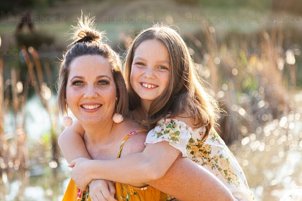Mother piggybacking daughter in park - Australian Stock Image