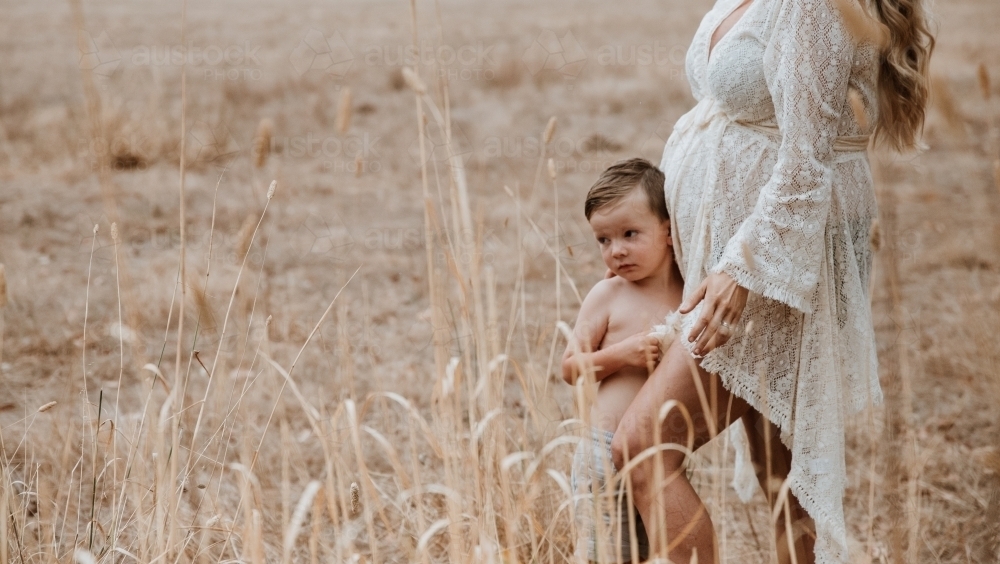 Mother pregnant with second child standing with son in brown grass outside - Australian Stock Image