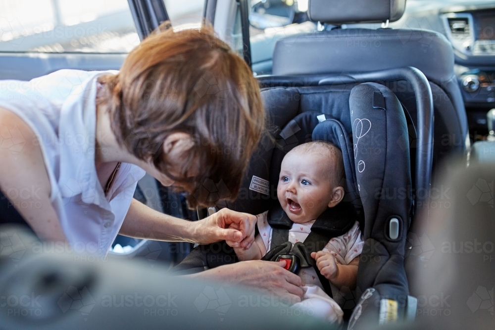Image of Mother putting baby in a car seat Austockphoto