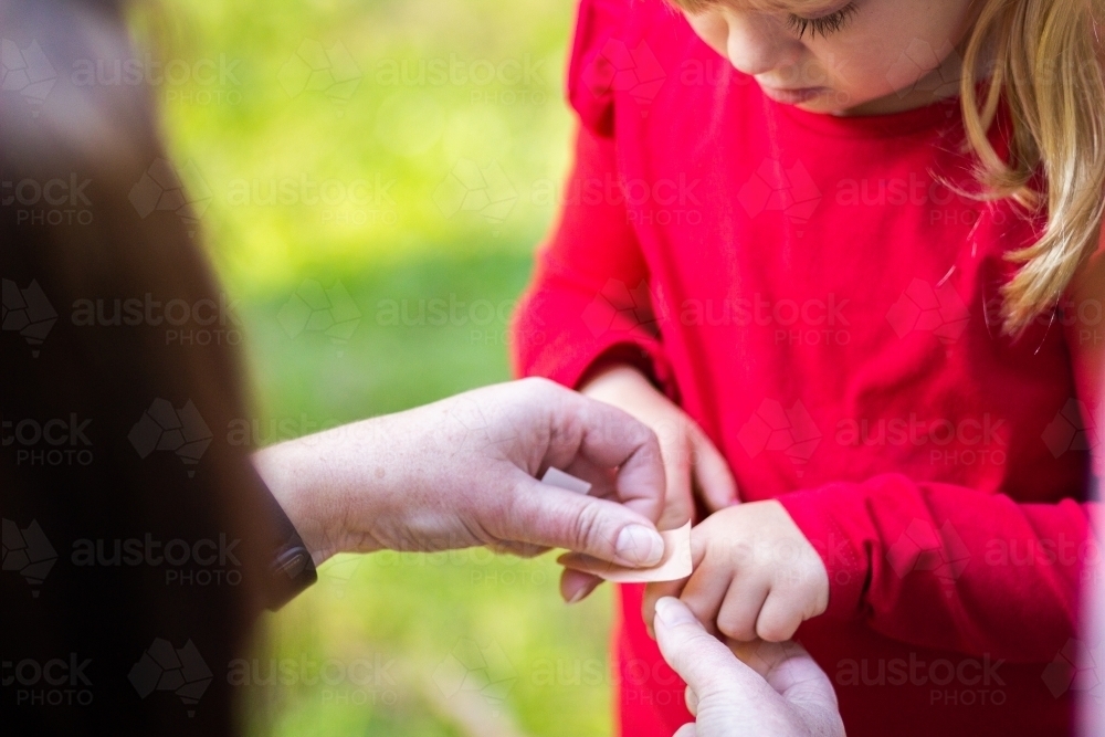 Mother putting band aid on child's cut finger - Australian Stock Image