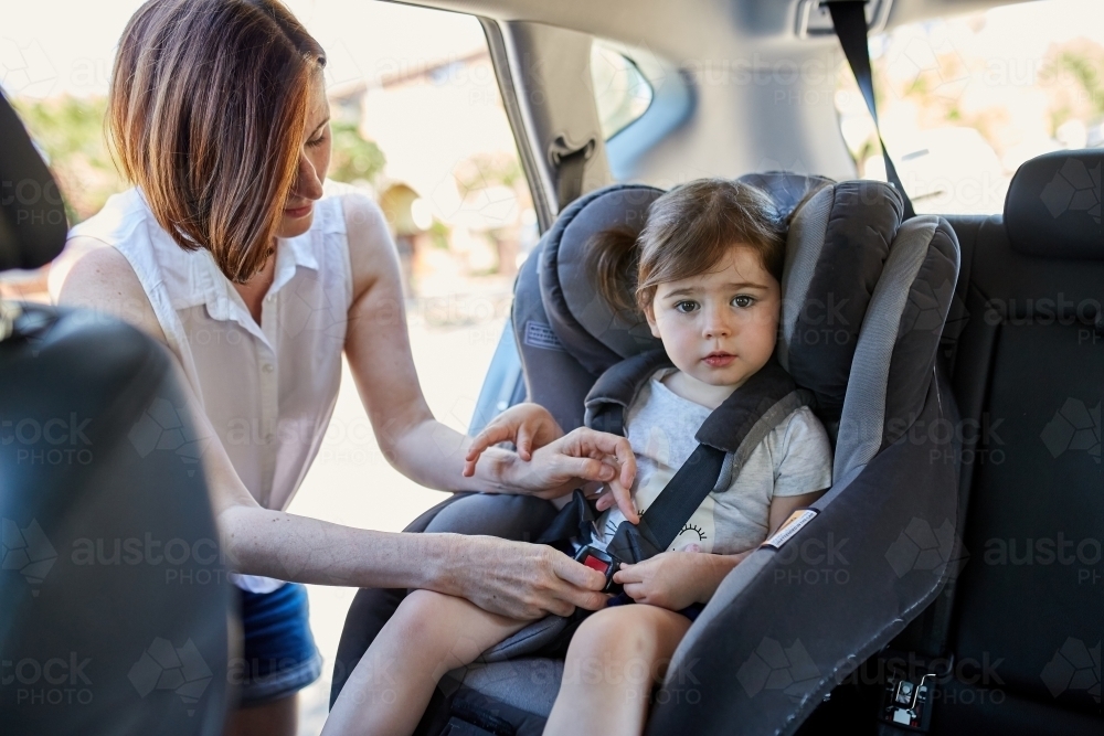 Mother putting daughter in forward facing car seat - Australian Stock Image
