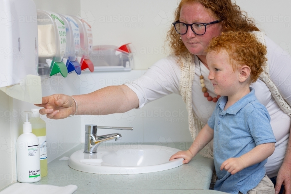mother reaching for paper towel to wipe child's hands clean - Australian Stock Image