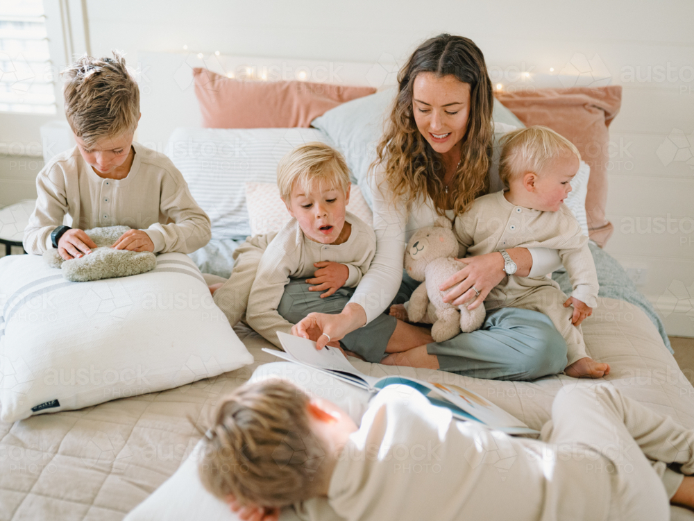 Mother reading a bedtime story with kids around the bed - Australian Stock Image